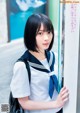A woman in a school uniform leaning against a wall.