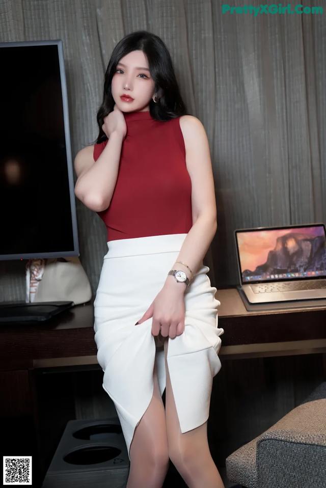 A woman in a red top and white skirt posing in front of a computer.