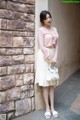 A woman leaning against a brick wall with a handbag.