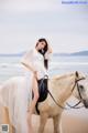 A woman in a white dress riding a white horse on the beach.