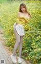 A woman in a yellow sweater and white skirt posing in a field of yellow flowers.