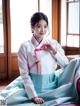 A woman in a blue and white hanbok sitting on a bed.