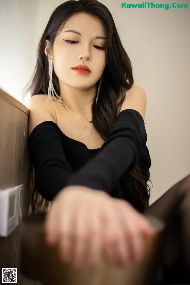 A woman in a black top leaning against a wall.