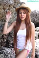 A woman in a straw hat leaning against a rock.