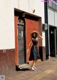 A woman in a black dress and straw hat standing in front of a building.