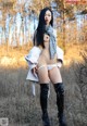 A woman in a white shirt and black boots posing in a field.